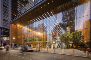 A dusk exterior view of the glowing glass lobby, highlighting the dramatic overhead lighting installations and the warm wood-slatted interior.