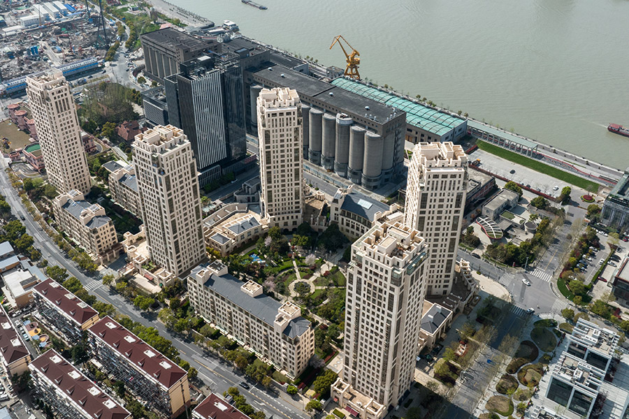 A birdseye view of a green park with a central water feature and paths coming off of its center, surrounded by four tall residential buildings.