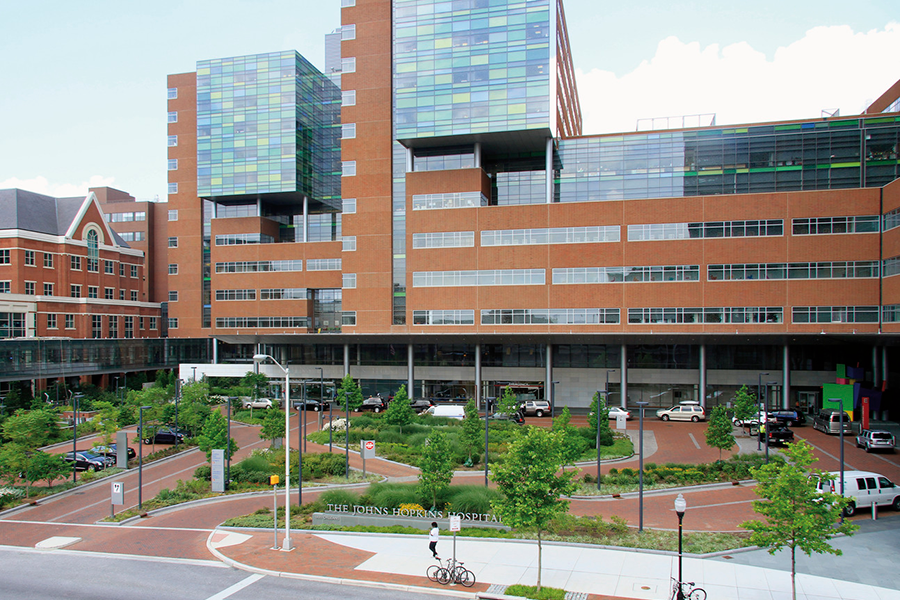 Wide view of the brick and glass facade of The Johns Hopkins Hospital, featuring a landscaped circular driveway and green space.