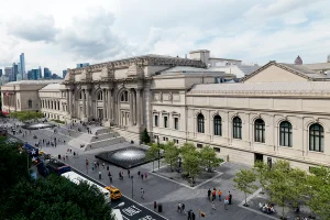High-angle view of the Metropolitan Museum of Art facade and the expansive David H. Koch Plaza with two circular fountains.