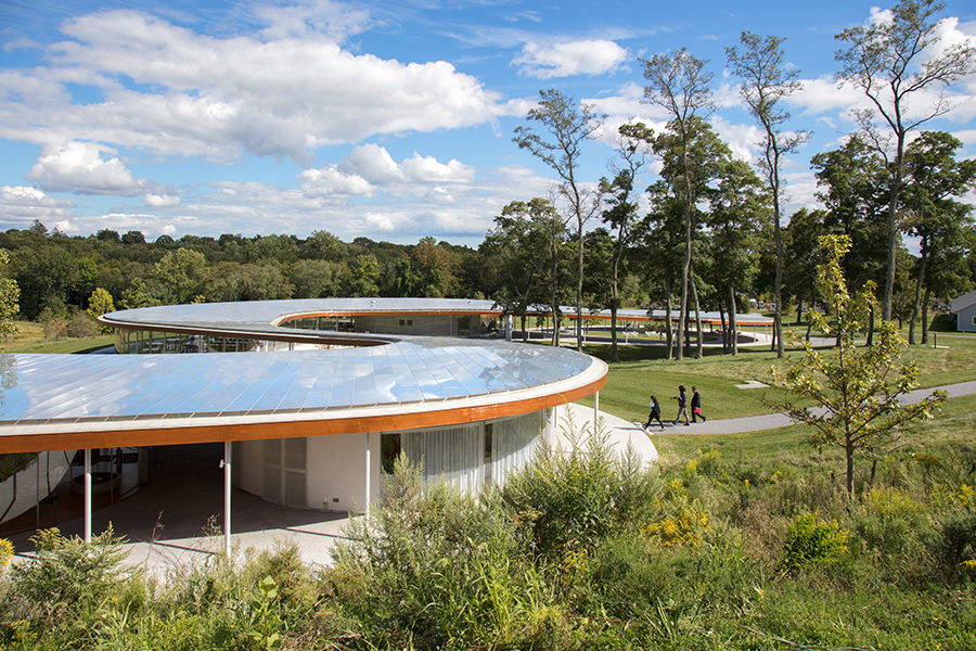 Elevated view of a serpentine building with a reflective roof winding through a wooded landscape.