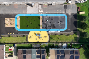 A direct top-down aerial view of the recreational complex, showing the symmetrical layout of the blue track, green field, basketball court, and yellow playground situated between a school building and a residential row.