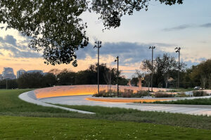 Wide view of the curved memorial plaza and softly lit earthwork wall at sunset.